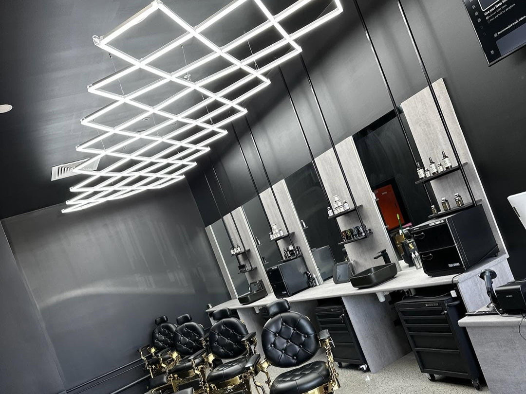 Diamond grid LED lights hung above mirror stations and gold barber chairs in a black barbershop
