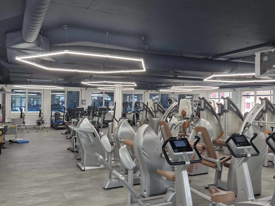 Large hexagon light frames hung on suspension wires above the training floor of a commercial gym