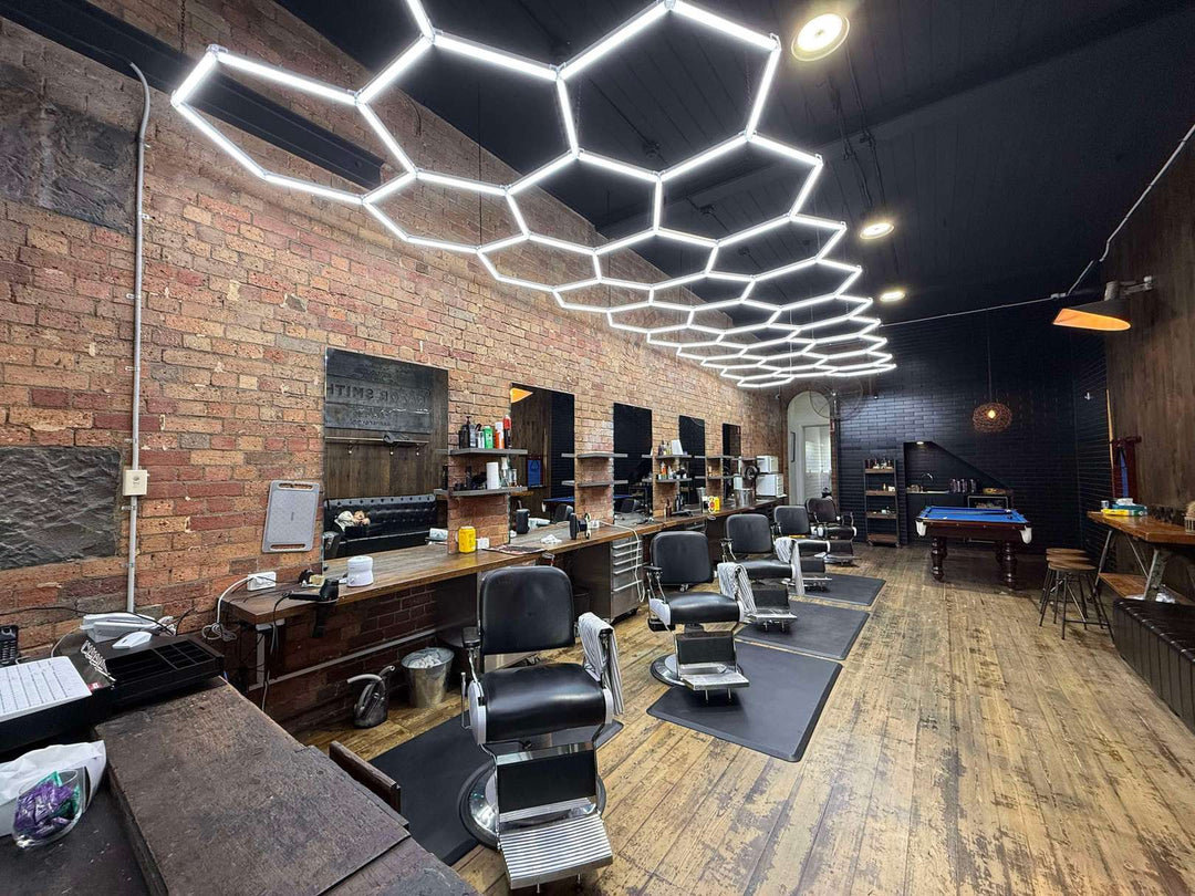 Barber shop with a red brick wall and a black ceiling, lit by a hexagon LED grid above a row of barber chairs