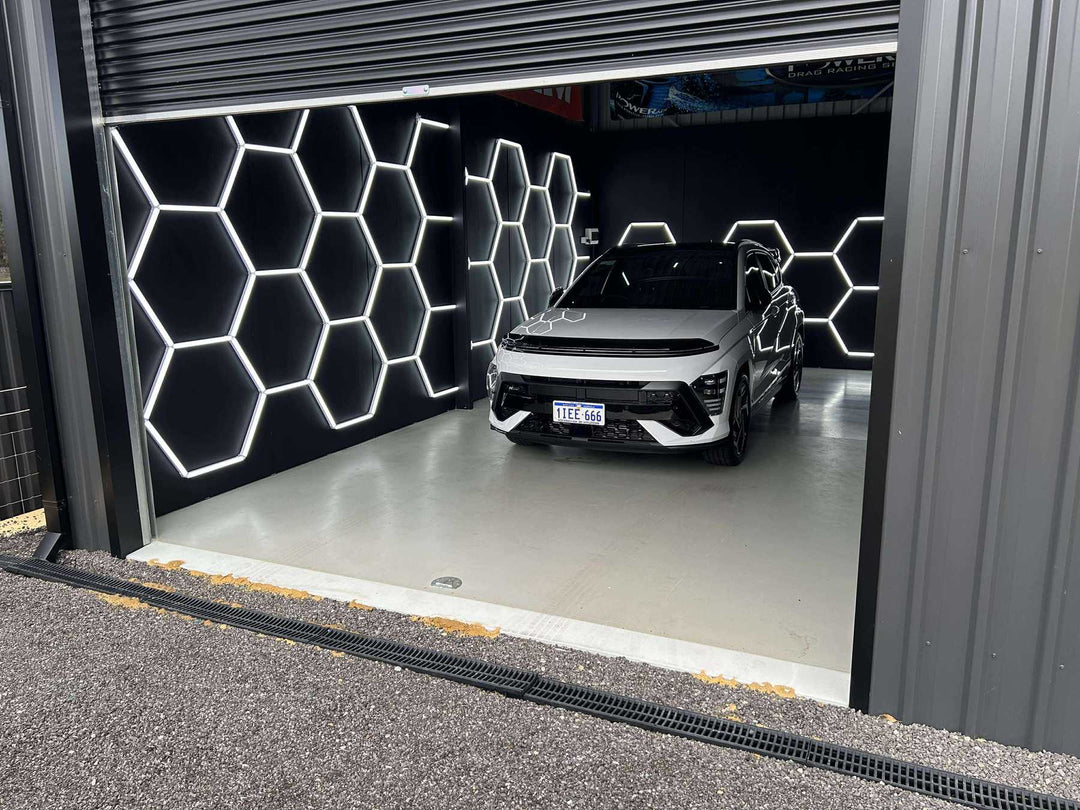 Hexagon lights mounted on the black back wall of a garage, lighting a parked silver SUV from behind