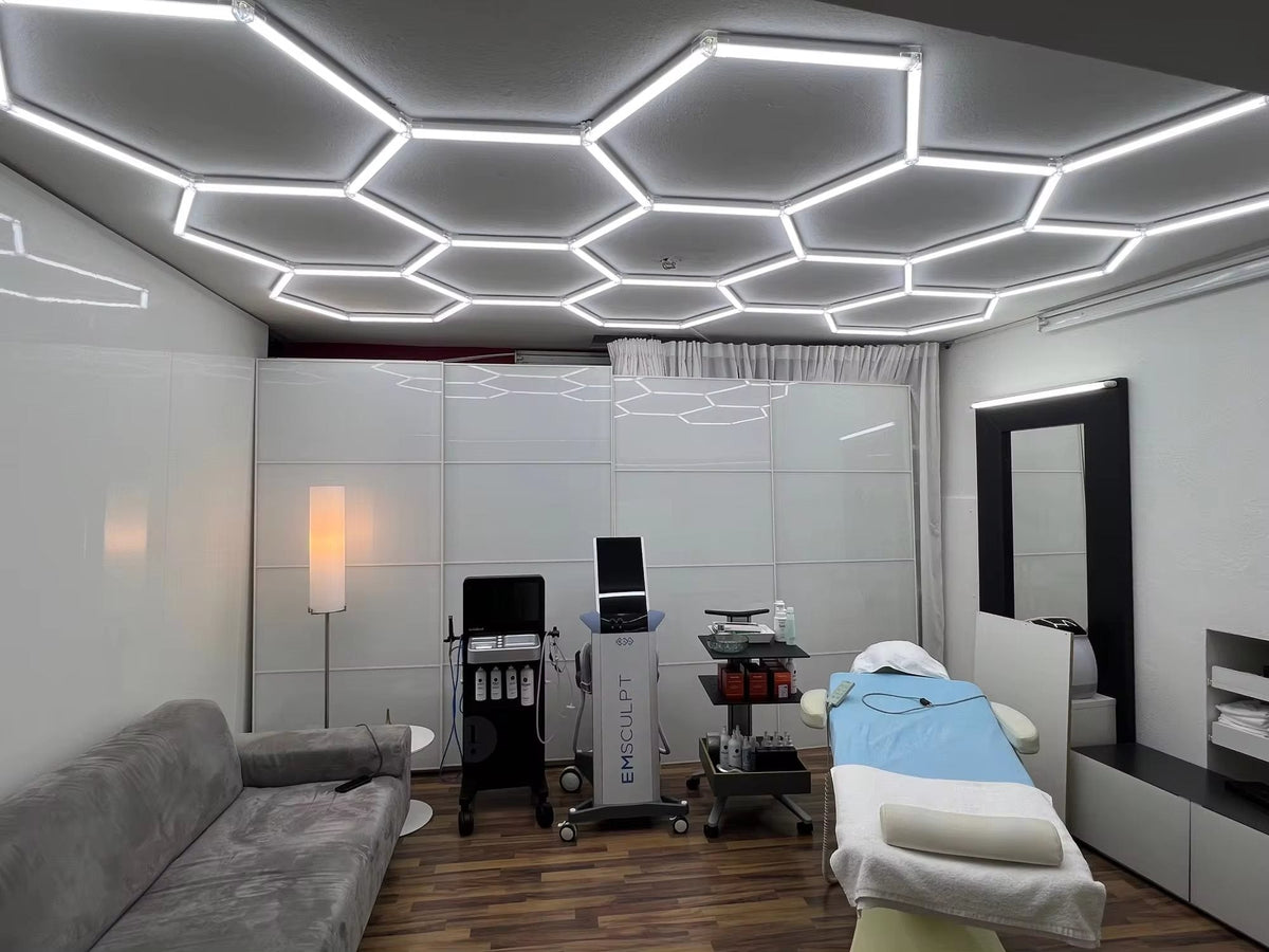 Treatment room with a full-ceiling hexagon LED grid above a treatment bed and a gray sofa