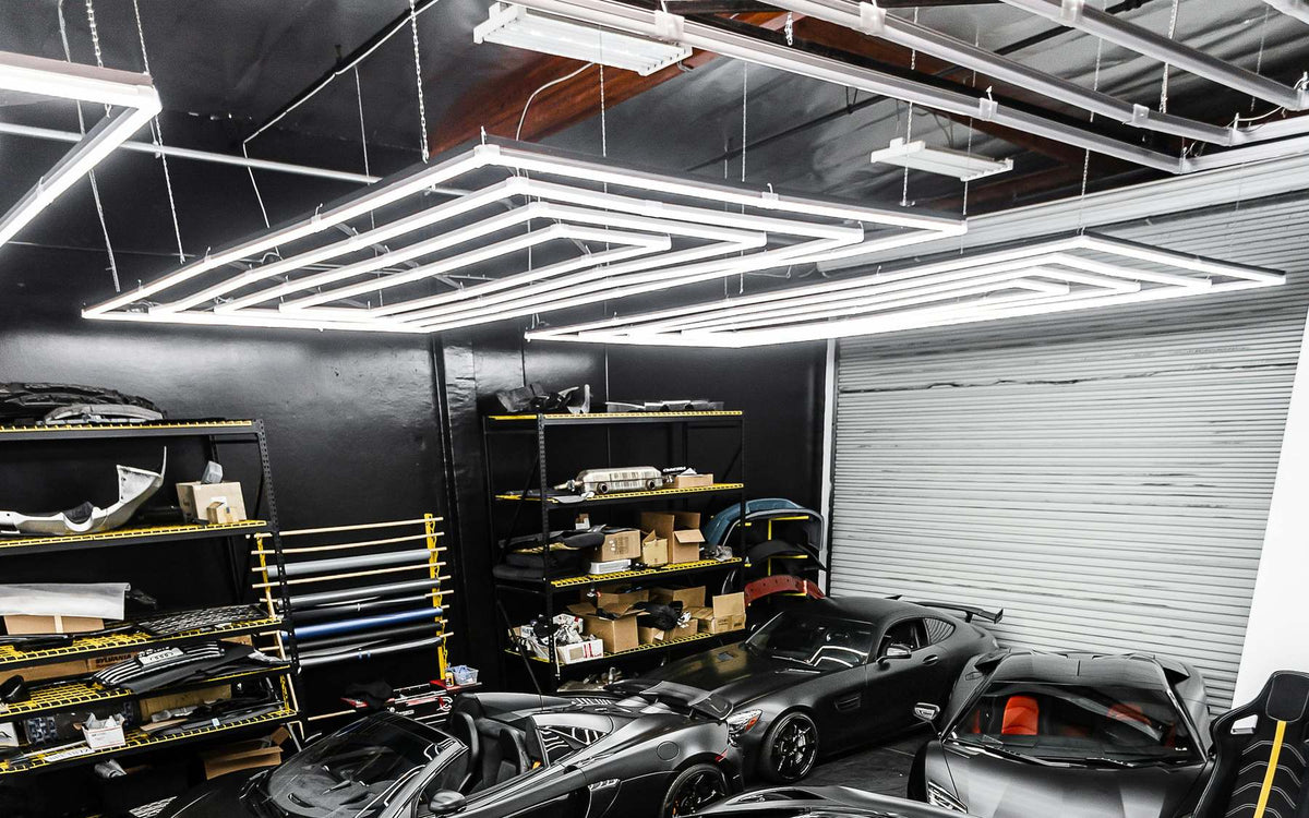 Nested linear frame lights hung above black sports cars in a tuning garage