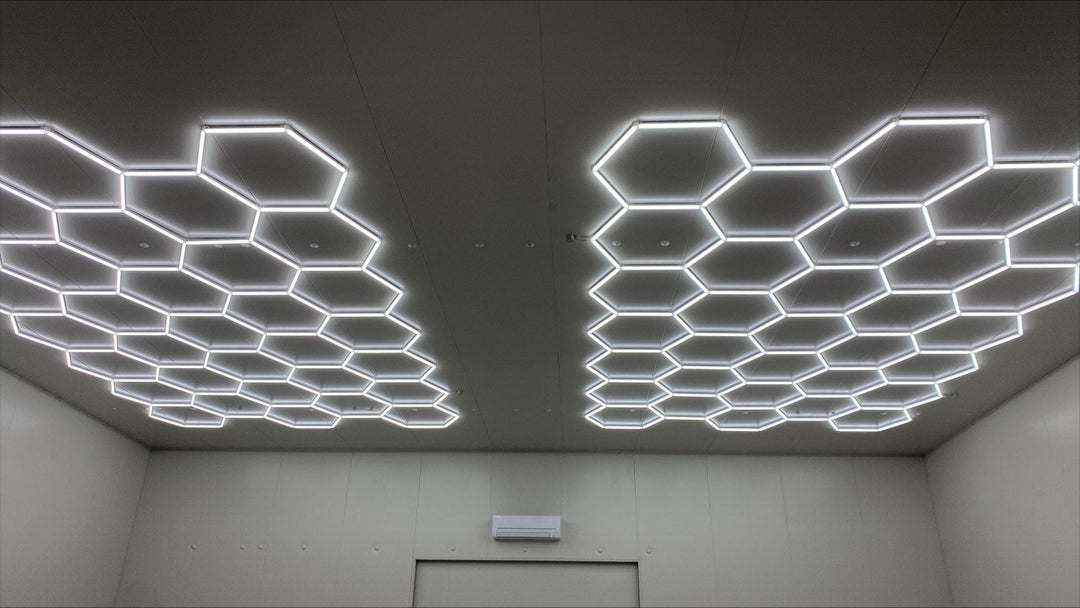 Two separate hexagon LED grids lighting one ceiling in an empty commercial room with gray walls