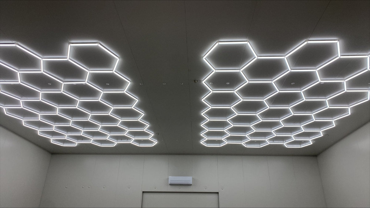 Two separate hexagon LED grids lighting one ceiling in an empty commercial room with gray walls