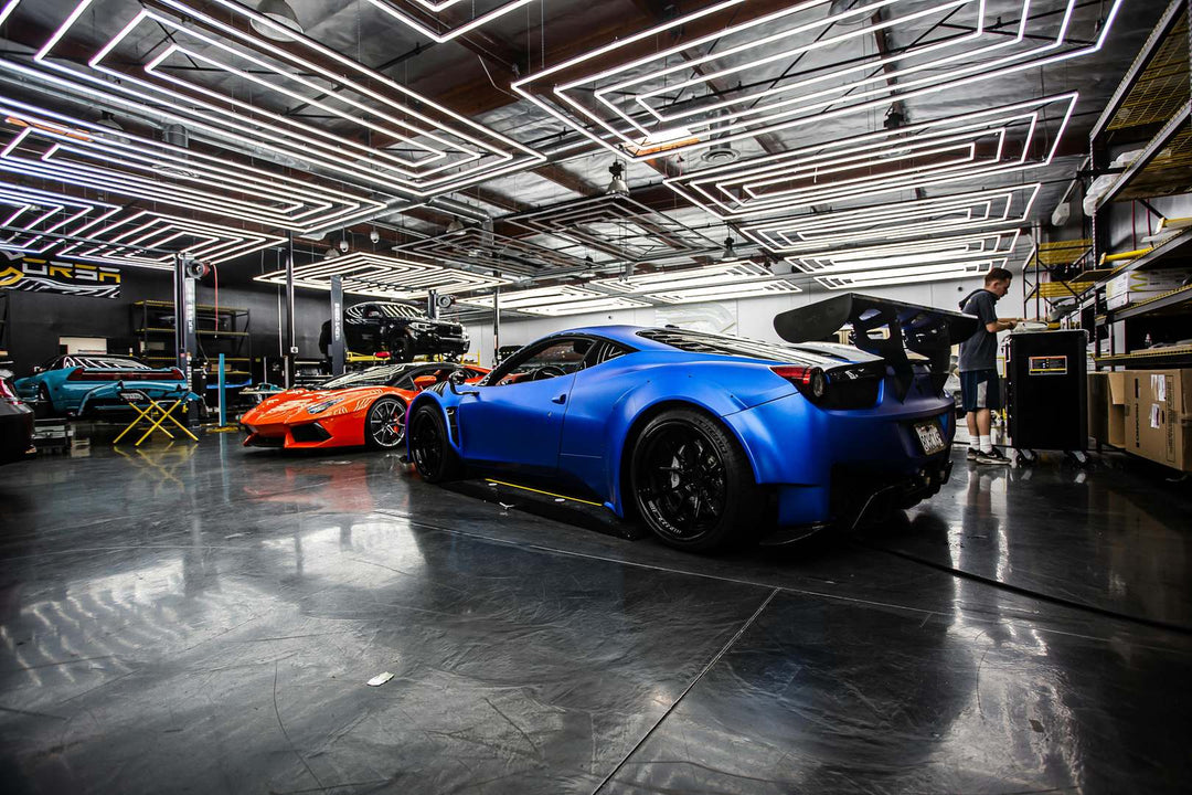 Rows of linear LED tubes across the ceiling of a car tuning workshop above blue and orange sports cars